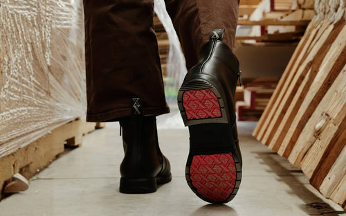 Xena Omega work boots with coral-accent outsole, worn beside stacked lumber