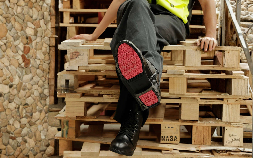 Xena Spice work boots with coral-accent outsole, worn beside stacked pallets
